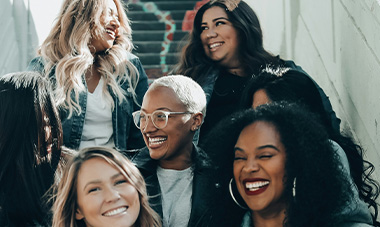 A diverse group of women smiling and enjoying each other's company in an urban setting.